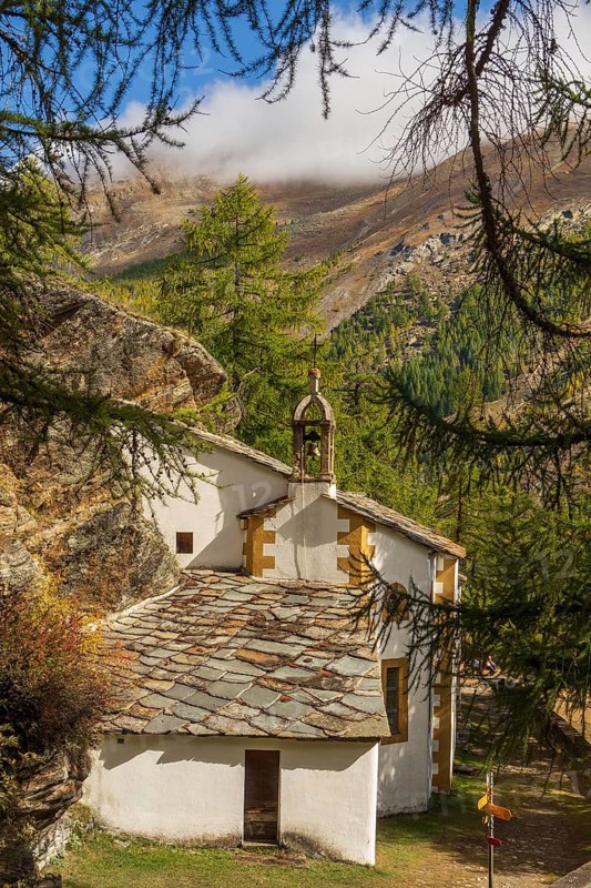 Small church with bell tower, surrounded by forest and mountains in an autumnal Alpine landscape, Saas Fee, Switzerland, Europe