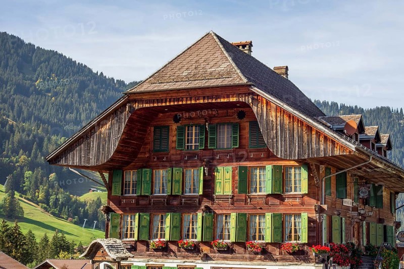 Red wooden house in the Alps with green shutters and flower boxes, surrounded by mountains in the background, Grisons, Switzerland, Europe