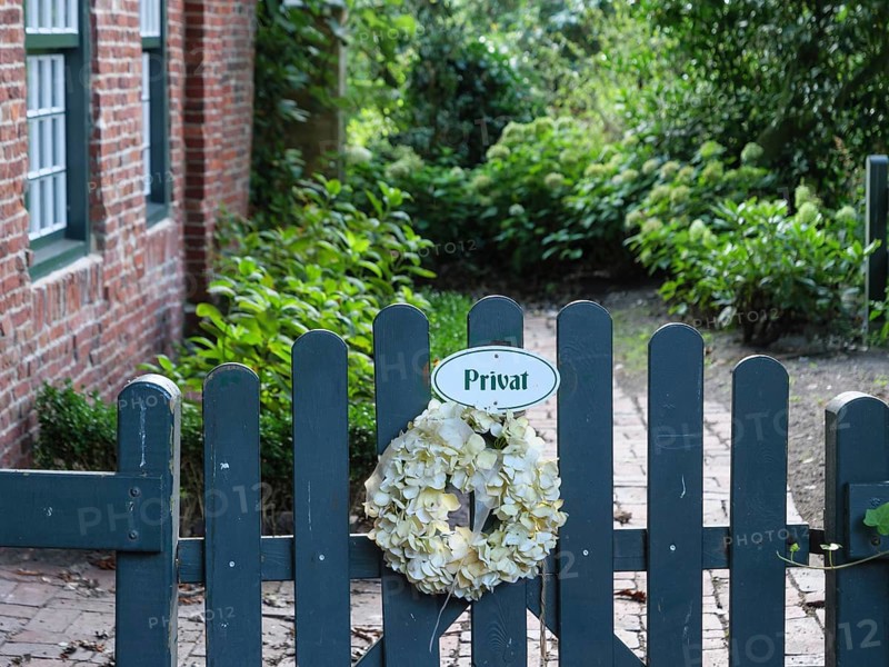 A garden fence with a 'Private' sign, decorated with a wreath of flowers, surrounded by plants, Spiekeroog, East Frisia, GERMANY