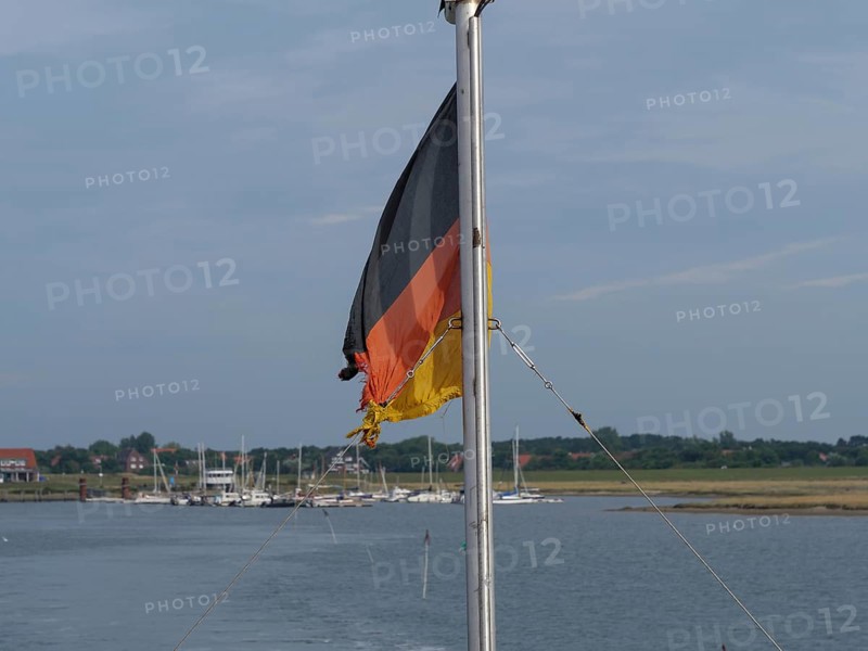A German flag on a boat, surrounded by water and a quiet harbour, Spiekeroog, East Frisia, GERMANY
