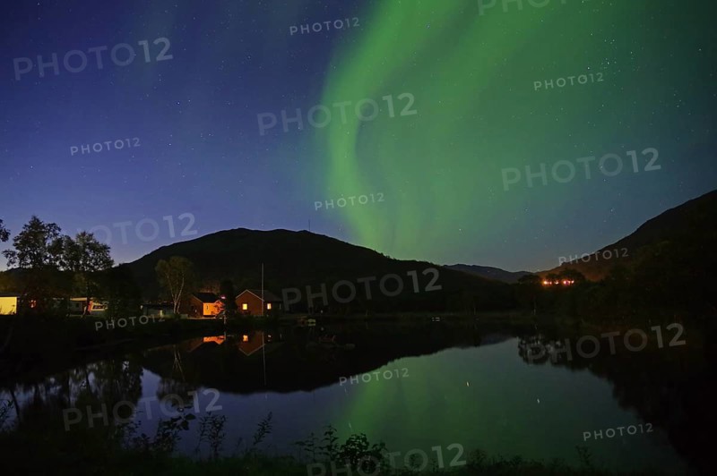 House and hill under the night sky with green northern lights and a reflection in the lake, Langöya, Vesteralen, Nordland, Norway, Europe