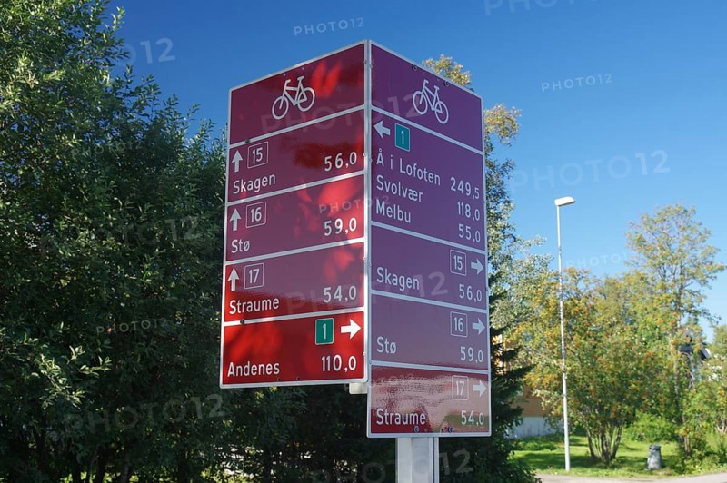 Red signpost with several bicycle symbols and distances in front of a green tree backdrop and clear sky, cycle tourism, Vesteralen, Nordland, Langoya, Norway, Europe