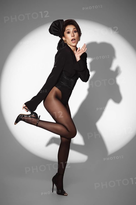 Beautiful woman in retro style in a black bodysuit and a bow in her hair in full length posing on a gray background. Beauty of body and face