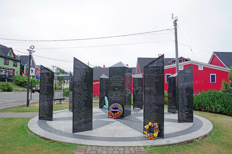 Circular memorial consisting of black plaques with texts, flowers at the base of the plaques, surrounded by urban scenery, memorial to the fishermen who did not return from the sea, Lunenburg, Nova Scotia, Canada, North America