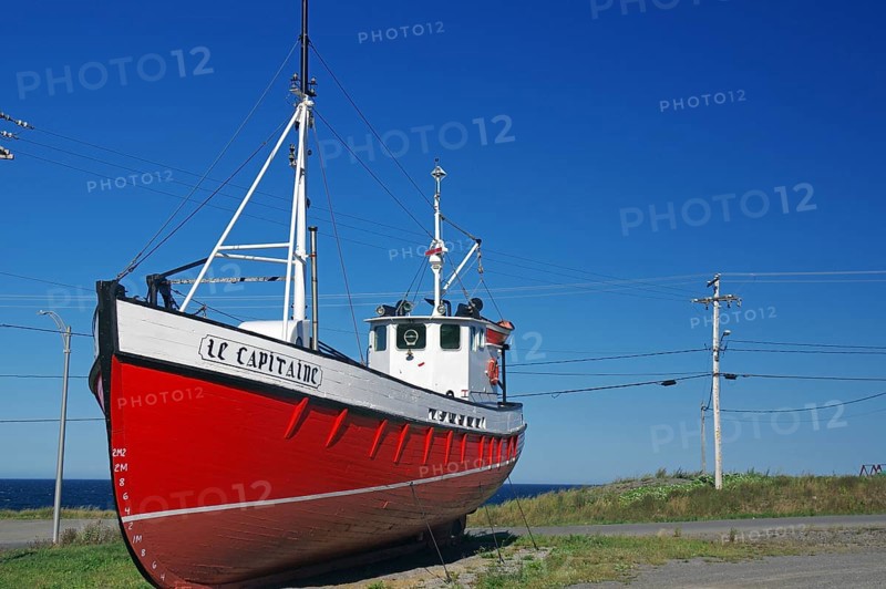 Red boat on land next to a coastal road under a clear blue sky, Gaspesie, St. Lawrence River, Quebec, Canada, North America