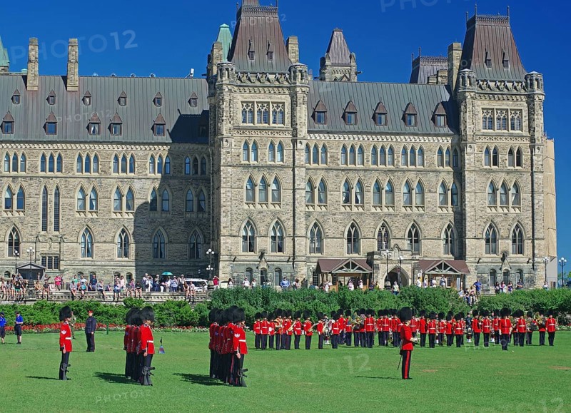 A group of uniformed soldiers march in front of a historic parliament building in sunny weather, Change of the guards, Ottawa, Ontario, Canada, North America