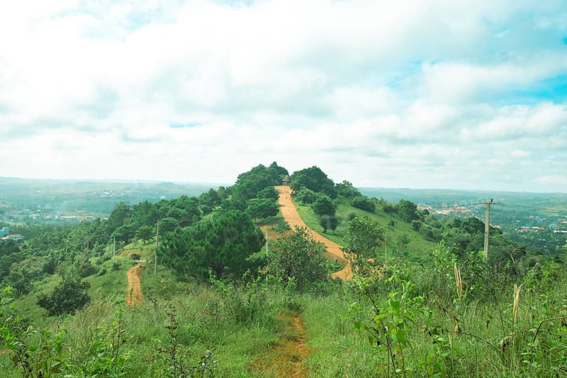 A serene hill with a winding path surrounded by lush greenery under a partly cloudy sky in the highlands of Mondulkiri, Cambodia, Asia