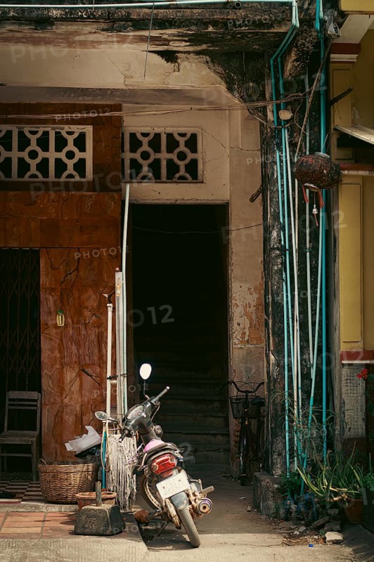 An old, weathered building entrance with a motorbike parked in front exuding a rustic and urban atmosphere showing the candid daily local khmer lifestyle in Kampot, Cambodia, Asia