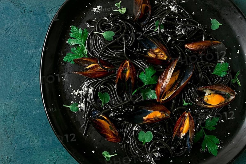 Spaghetti with black squid, black pasta, with boiled mussels, on a black plate, with parsley and parmesan cheese, close-up, selective focus, no people