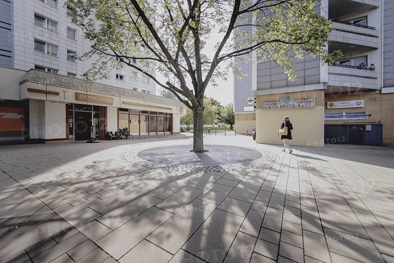 A woman walks next to a tree along a prefabricated building, taken in Berlin, 07/08/2024