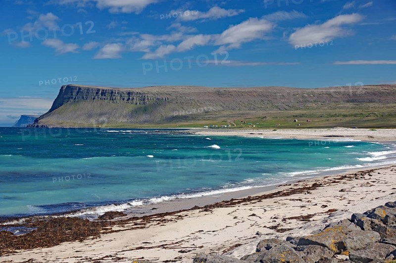 A clear day on a sandy beach with waves crashing against the shore and sapphire blue water, Latrabjarg, Vestfirdir Peninsula, Iceland, Europe