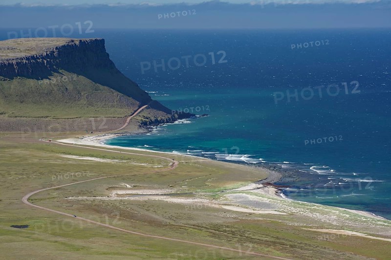A cliff juts out over the deep blue sea, next to a long, sandy beach and green meadows, Latrabjarg, Vestfirdir Peninsula, Iceland, Europe