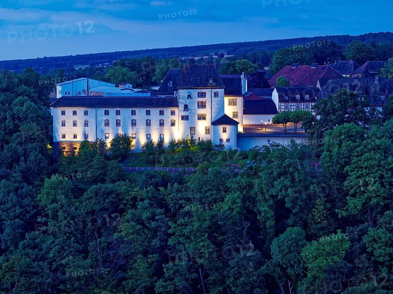 Fürstenberg Castle, a Spornburg, illuminated at night, lies on the Karthagenberg above the Weser valley. Aerial photo. Fürstenberg, Lower Saxony, Germany, Europe