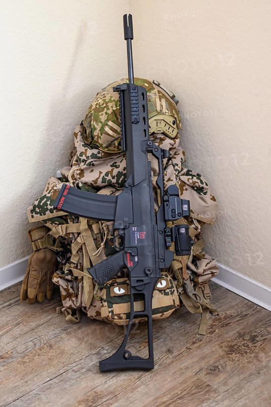 Rifle and military equipment with camouflage pattern, including a rucksack, placed in front of a light-coloured wall on a hard wooden floor, mobilisation, Bundeswehr