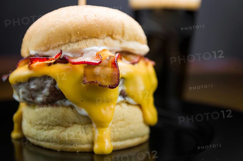 Close-up of tasty homemade bacon burger and cheddar sauce on wooden table and black background