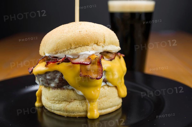 Close-up of tasty homemade bacon burger and cheddar sauce on wooden table and black background