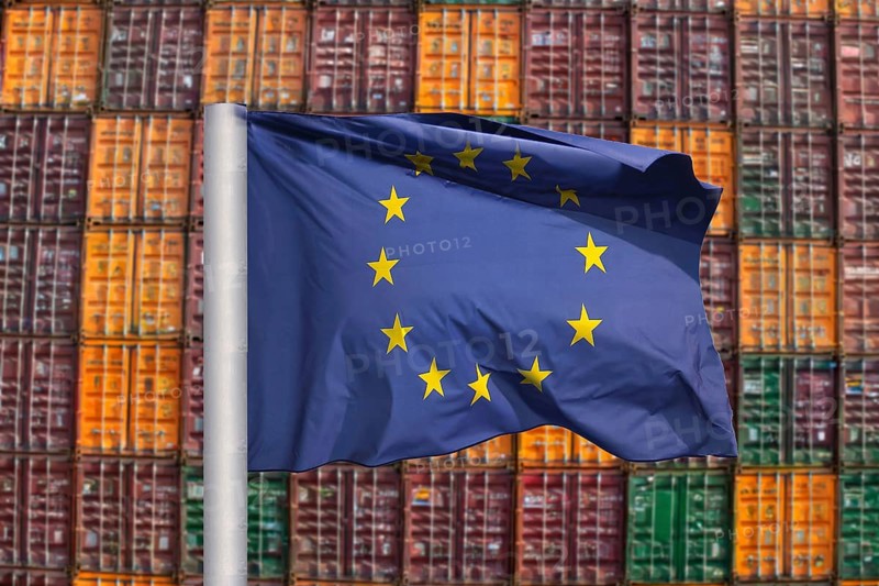 Symbolic image of the economy in the EU: EU flag in front of a large stack of shipping containers (Composing)