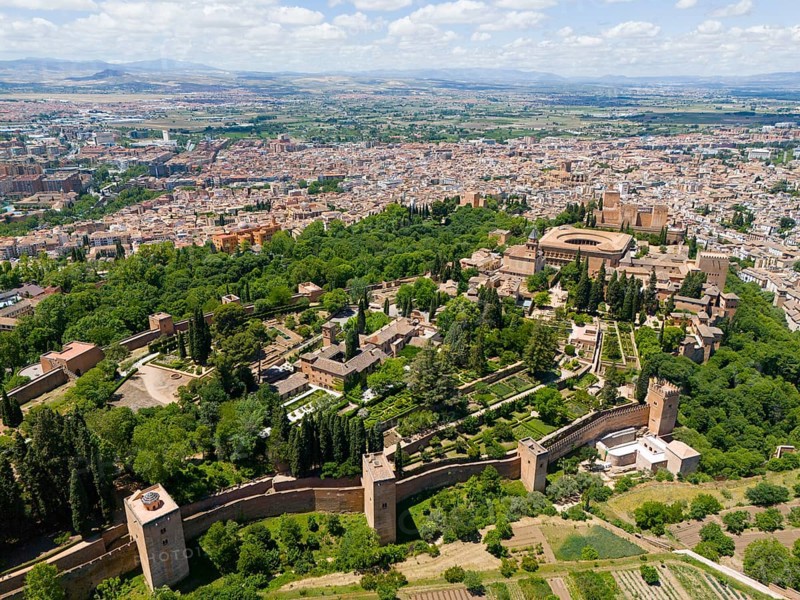 Aerial view of a castle complex surrounded by green trees and bordering an urban landscape with fields, Aerial view, Alhambra, Andalusia, Granada, Spain, Europe
