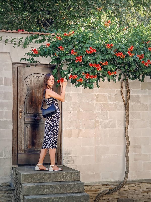 Young woman enjoys a beautiful summer day in vacation standing at the threshold of a door smelling orange creepers trumpet flowers (Campsis radicans)