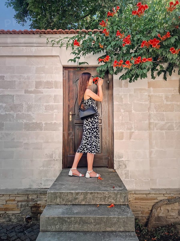 Young woman enjoys a beautiful summer day in vacation standing at the threshold of a door smelling orange creepers trumpet flowers (Campsis radicans)