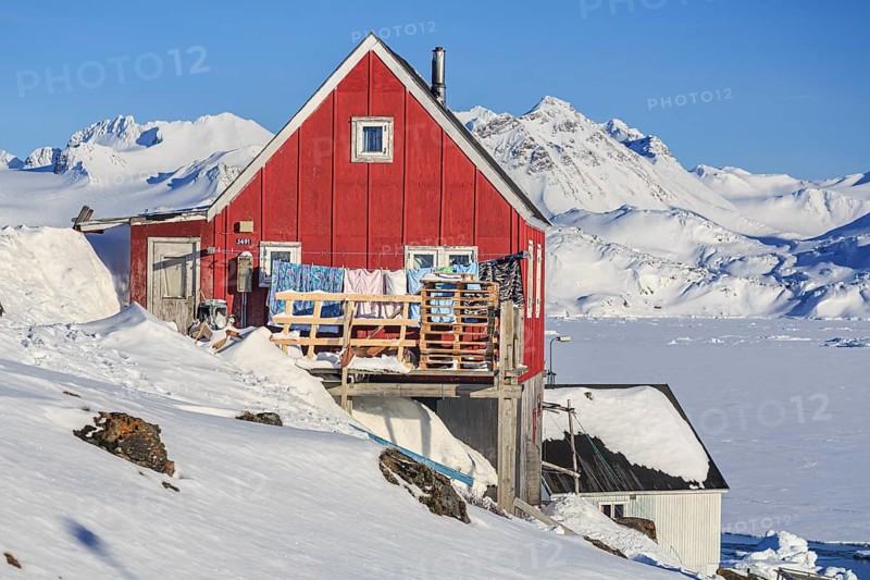Typical Greenlandic house in front of fjord and snowy mountains, sunny, Inuit settlement, winter, Arctic, Kulusuk, East Greenland, Greenland, North America