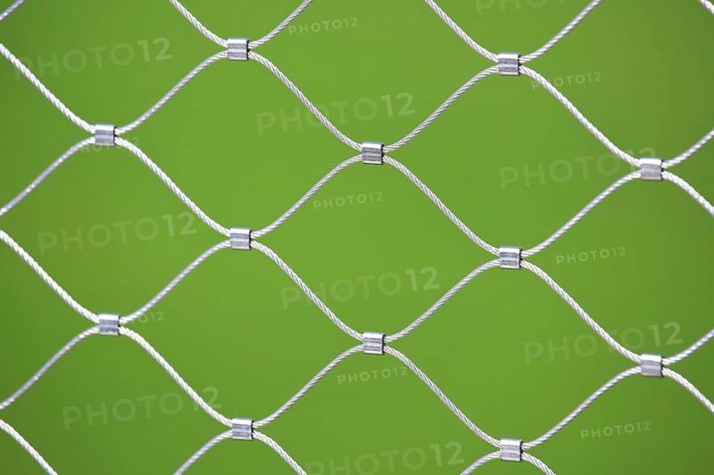 Mesh screen made of interwoven metal cables. The background is a uniform green colour. This image could be interesting as a metaphor for networked systems and networks