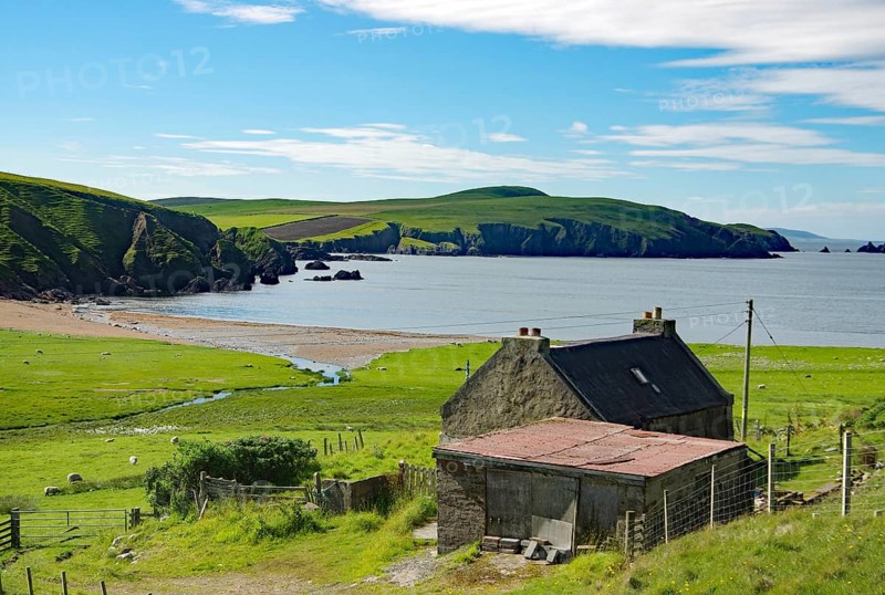 Coastal landscape with a small house near the sea, green hills and beach under a cloudy sky, crime film location, Shetland Islands, Scotland, United Kingdom, Europe