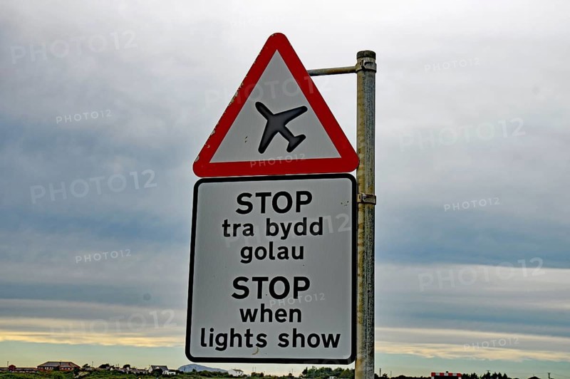 Road sign with an aeroplane symbol and bilingual text in a rural landscape under a cloudy sky, Shetland Islands, Scotland, United Kingdom, Europe