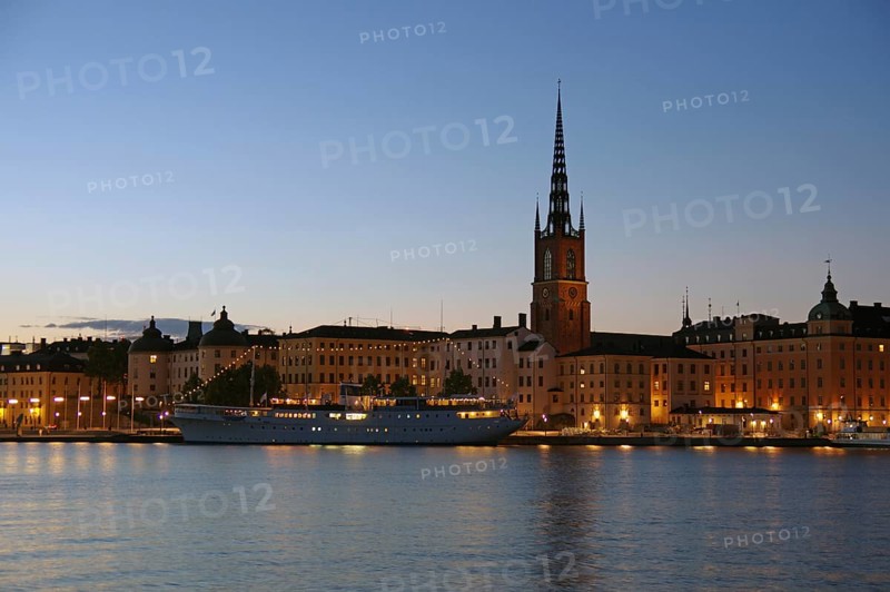 Idyllic evening view of an illuminated church and buildings along the water with a quiet shore, Gamla Stan, Old Town, Stockholm, Sweden, Europe