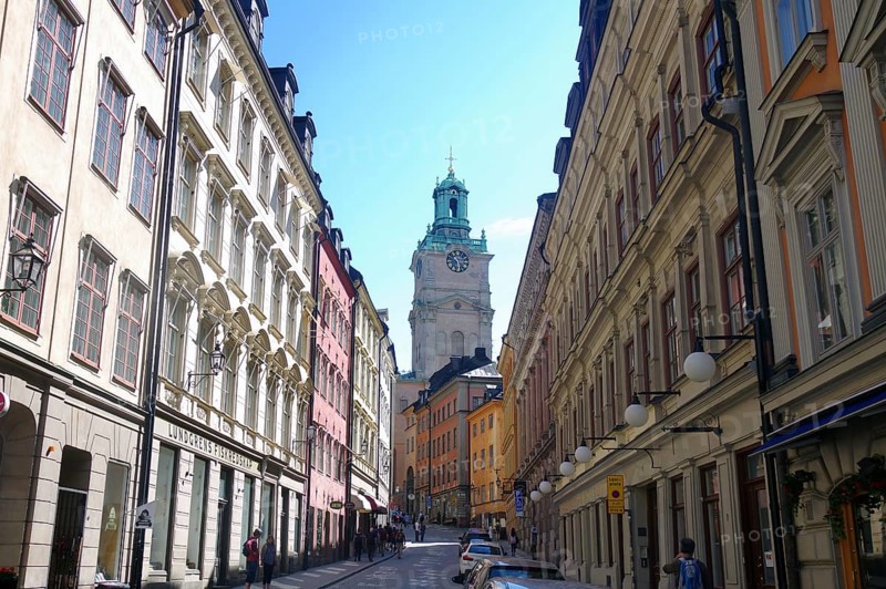 Narrow street between tall, pastel-coloured buildings with a view of a church tower on a sunny day, Gamla Stan, Old Town, Stockholm, Sweden, Europe