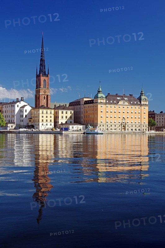 Picturesque view of a church tower and historic buildings along a calm shore with clear water reflection under a sunny sky, Gamla Stan, Old Town, Stockholm, Sweden, Europe