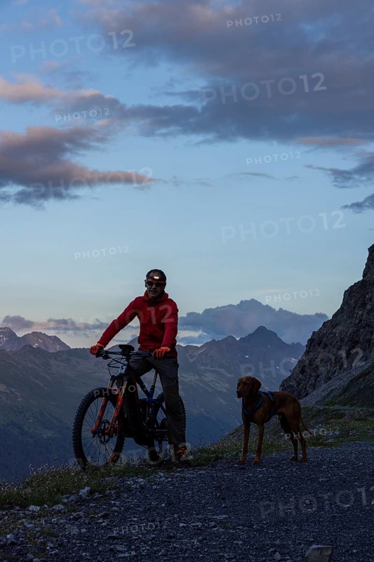 Mountain biker with headlamp, with trail dog in the evening, man with his Vizsla, panoramic trail, Davos, Grisons, Switzerland, Europe
