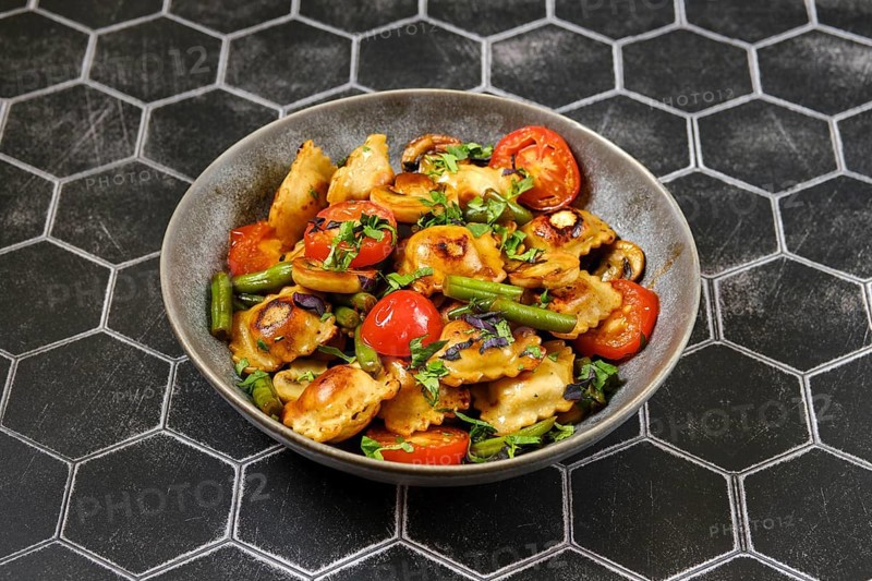 Fried ravioli with green beans, tomato and champignon mushrooms in a plate