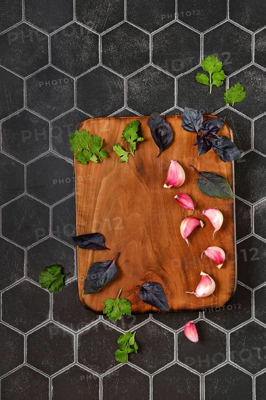 Overhead composition with place for text with wooden chopping board with basil, garlic and cilantro