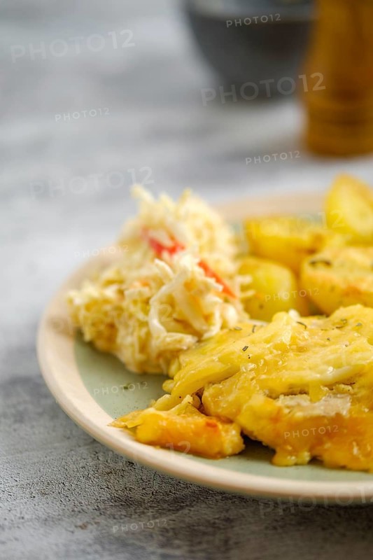 Close-up view of baked pork fillet with melted cheese served with fried potato and cabbage salad