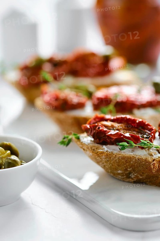 Close-up view of bruschetta with sun-dried tomatoes and capers on marble serving board