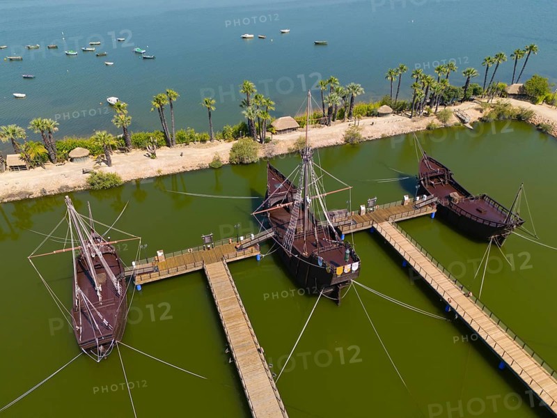 Several historic sailing ships in a water basin surrounded by tropical palm trees under a clear sky, aerial view, Muelle de las Carabelas, reproductions of La Nina, La Pinta and La Santa Maria, Museum, Palos de la Frontera, Province of Huelva, Andalusia, Spain, Europe