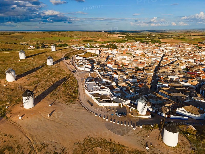 Aerial view of windmills near a village in sunny weather with blue sky and clouds. The white buildings and green fields characterise the scene. Aerial view, windmills, Campo de Criptana, province of Ciudad Real, Castilla-La Mancha, Route of Don Quixote, Spain, Europe