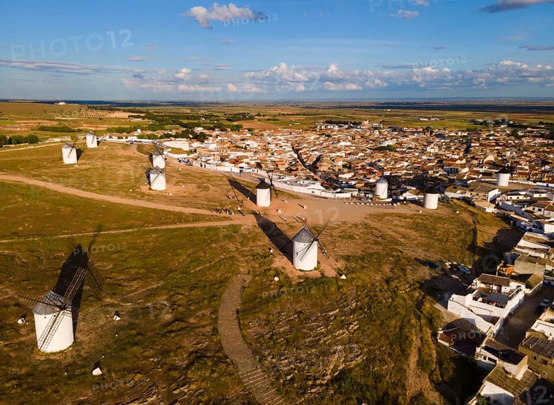 Windmills scattered on a hill near a village in sunny weather with blue skies and clouds. The surroundings are green and spacious. Aerial view, windmills, Campo de Criptana, province of Ciudad Real, Castilla-La Mancha, Route of Don Quixote, Spain, Europe