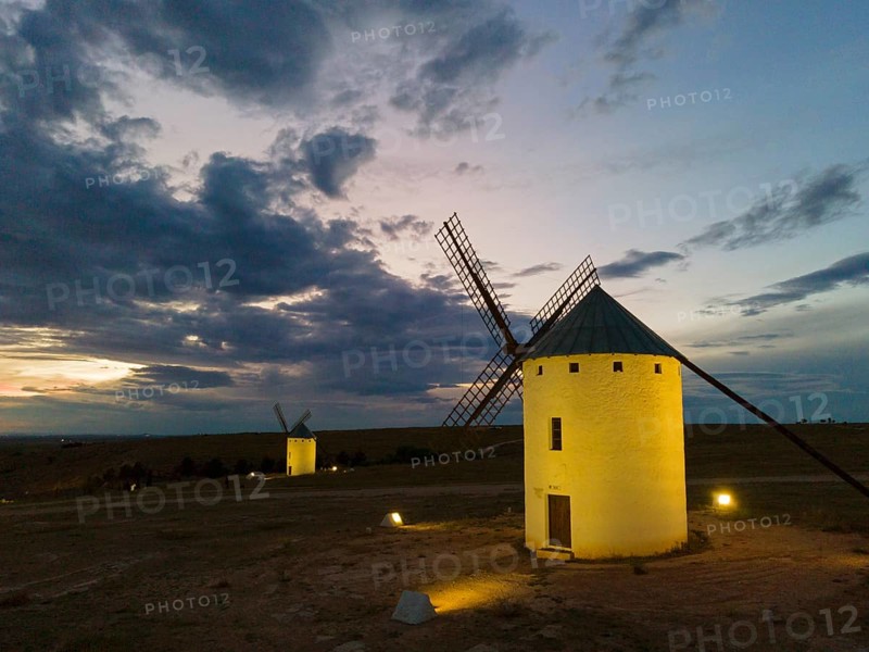 An illuminated windmill at night under a cloudy sky. The surroundings appear calm and quiet, while the mill shines in the soft light. Aerial view, windmills, Campo de Criptana, province of Ciudad Real, Castilla-La Mancha, Route of Don Quixote, Spain, Europe