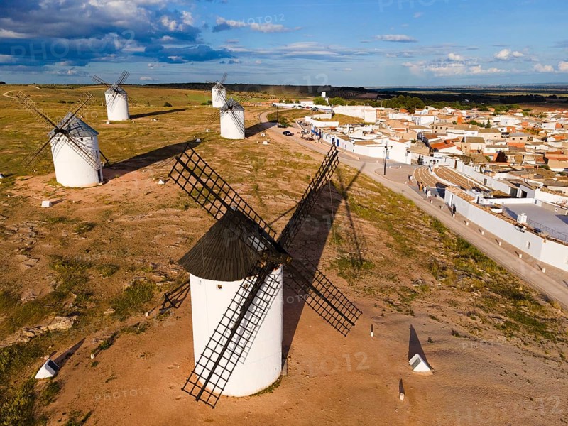 Windmills in a rural setting in sunny weather with blue sky and clouds. In the background a village with white houses and red roofs. Aerial view, windmills, Campo de Criptana, province of Ciudad Real, Castilla-La Mancha, Route of Don Quixote, Spain, Europe