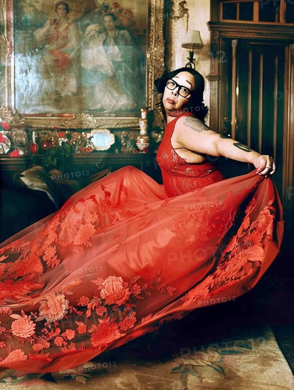 Woman in a flowing red dress with floral patterns, in an ornate and luxurious room featuring a vintage painting, AI generated
