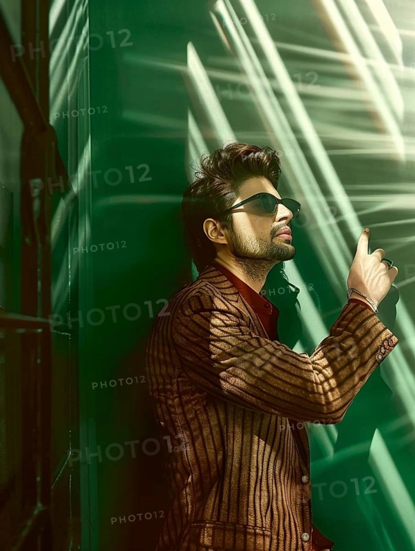 Stylish man in sunglasses and a striped jacket leaning against a green wall, lit by sunlight and shadows, AI generated