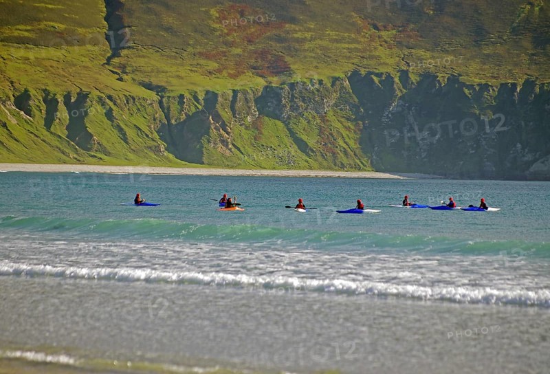 Group of surfers on their boards on the sea near rocky shore, Achill Island, County Mayo, Ireland, Europe