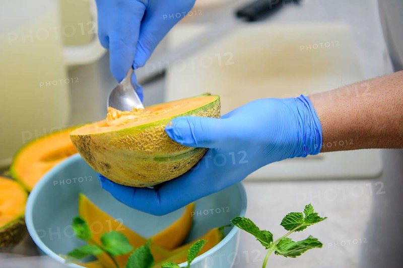 Person preparing cantaloupe with a spoon in the kitchen, highlighting food preparation, hand hygiene, and fresh ingredients