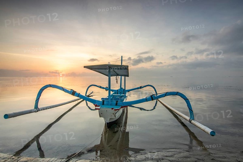 Fantastic sunrise on the beach with small temples and a traditional fishing boat, Jukung. View of the sea as far as the horizon. Sanur, Bali, Indonesia, Asia