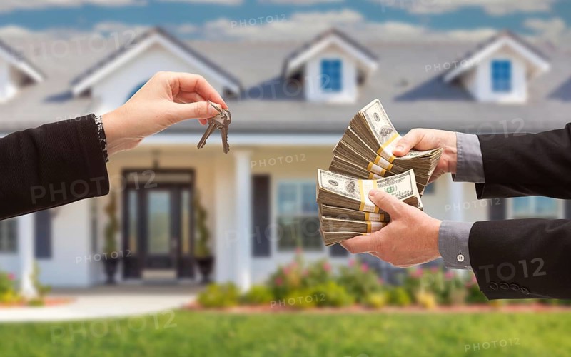 Real estate agent handing over house keys for stacks of money in front of new house