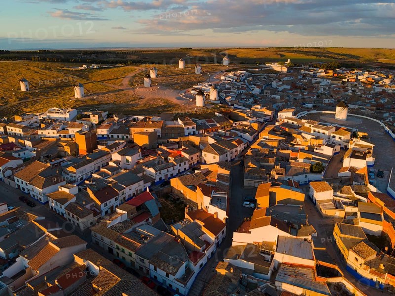 Roofs and houses of a village at dusk with windmills in the background and orange lighting, aerial view, windmills, Campo de Criptana, Ciudad Real province, Castilla-La Mancha, Route of Don Quixote, Spain, Europe