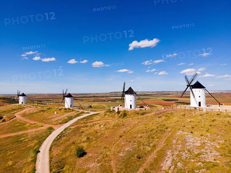 Several white windmills stand along a dirt road under a clear blue sky, aerial view, Alcazar de San Juan, Ciudad Real, Castilla-La Mancha, Route of Don Quixote, Spain, Europe