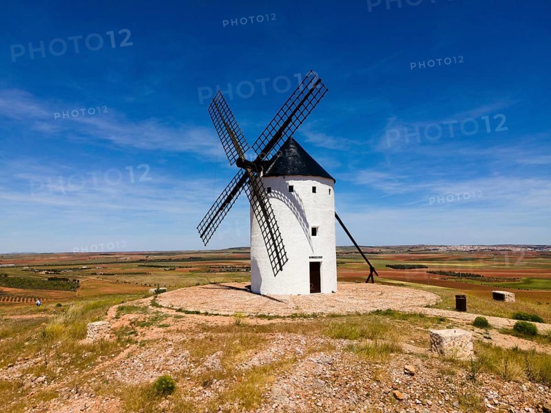 A lone white windmill stands in a field under a bright blue sky, aerial view, Alcazar de San Juan, Ciudad Real, Castilla-La Mancha, Route of Don Quixote, Spain, Europe